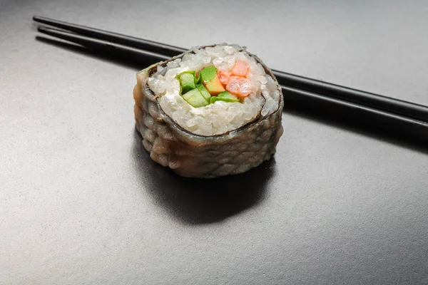 Rotolo di sushi caldo su una superficie nera lucida con riflesso sfocato e posto per testo — Foto Stock