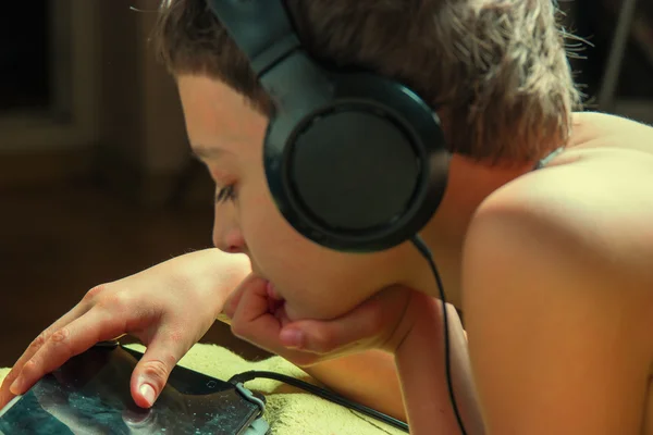 Ragazzo che ascolta musica o ha un corso di e-learning sul suo tablet collegato a un paio di cuffie, vista laterale, immagine tonica, messa a fuoco a portata di mano — Foto Stock