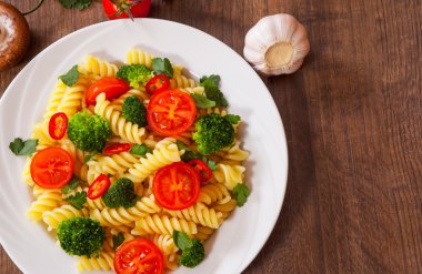 Düdük makarna domates ve brokoli ahşap masa üzerinde bir plaka ile