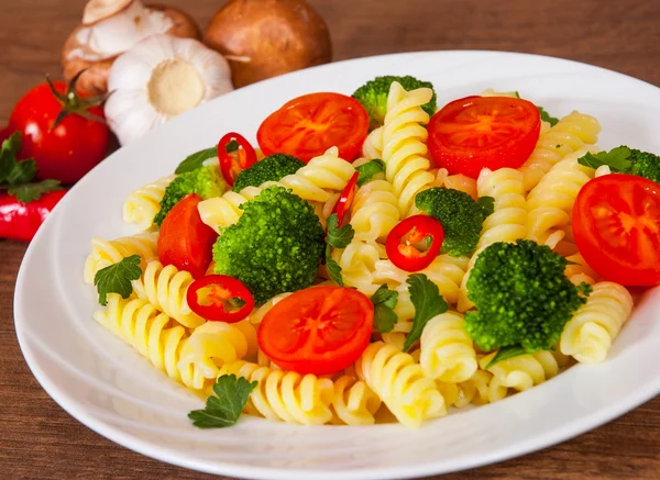 Düdük makarna domates ve brokoli ahşap masa üzerinde bir plaka ile