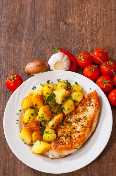 Жареная куриная грудка с картошкой в тарелке на деревянном столе — стоковое фото