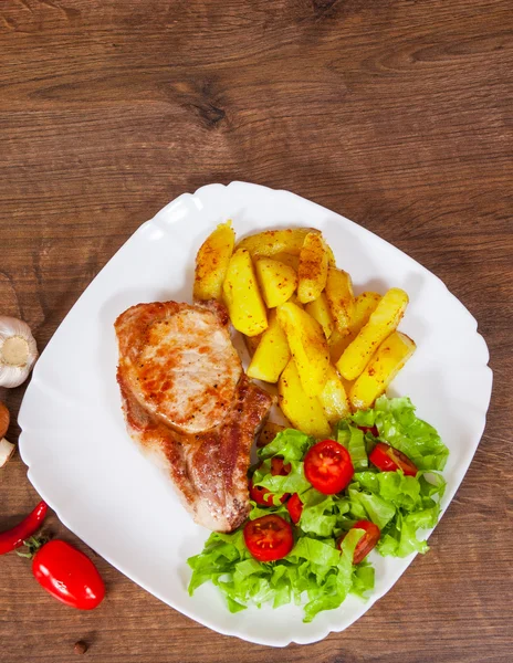 Bife de filé de carne grelhada suculento com salada de batata frita e legumes em uma placa na mesa de madeira — Fotografia de Stock