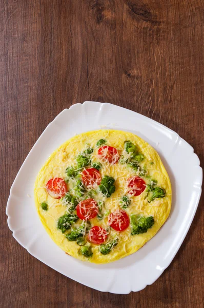 Omelet with tomato, broccoli and cheese in a plate on wooden table — Stock Photo, Image