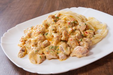 Ahşap masa üzerinde bir tabak spagetti makarna ile krem soslu kızarmış tavuk eti dilimlenmiş
