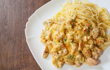 Ahşap masa üzerinde bir tabak spagetti makarna ile krem soslu kızarmış tavuk eti dilimlenmiş