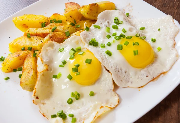 Spiegeleier mit Kartoffeln im Teller auf Holztisch — Stockfoto