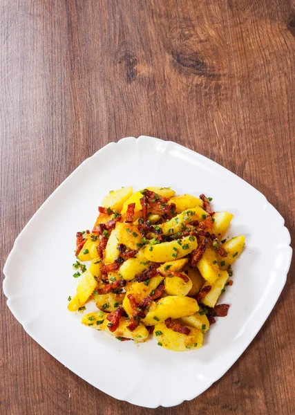 Stekt potatis med bacon i en platta på träbord — Stockfoto