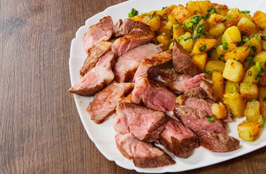 Ahşap masa üzerinde bir tabak içinde orta nadir ızgara biftek antrikot patates ile dilimlenmiş