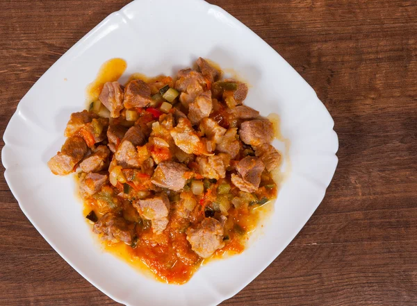 Geschmortes Fleisch mit Gemüse in einem Teller auf einem Holztisch — Stockfoto