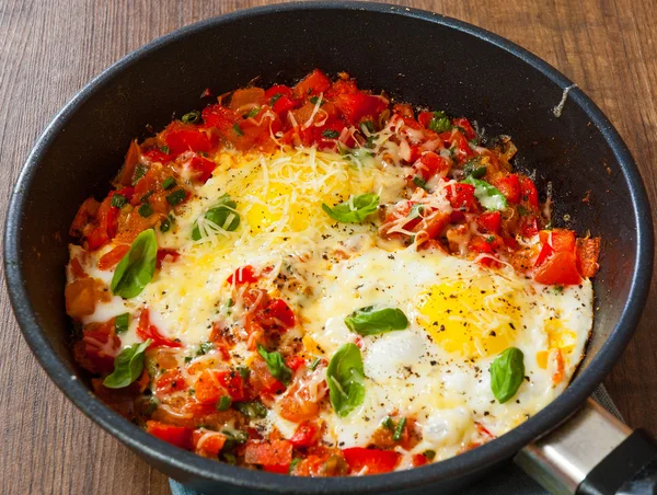 Fried eggs with vegetables and cheese in a frying pan on wooden table — Stock Photo, Image