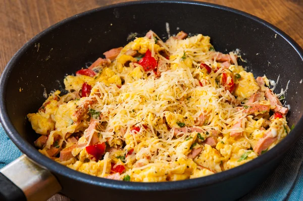 Scrambled eggs with ham, vegetables and cheese in a frying pan on wooden table — Stock Photo, Image