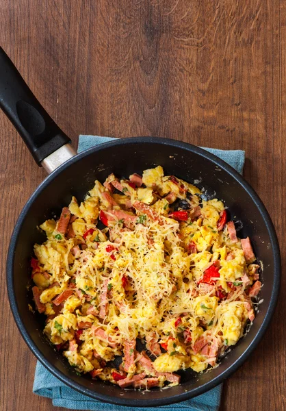 Scrambled eggs with ham, vegetables and cheese in a frying pan on wooden table — Stock Photo, Image