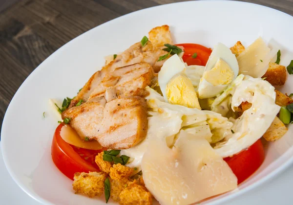 Caesar salade met croutons, kaas, eieren, tomaten en gegrilde kip op houten tafel — Stockfoto