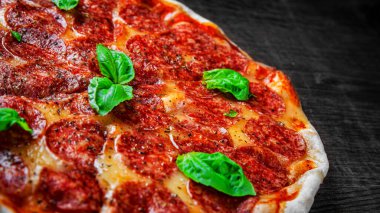 Mozzarella peynirli biberli pizza, salam, domates sosu, biber, baharat ve taze fesleğen. İtalyan pizzası ahşap masa arkasında