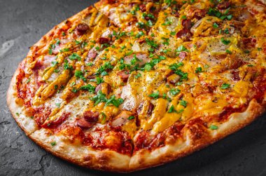 Mozzarella peynirli pizza, salam, domates sosu, biber, sosis, salatalık turşusu ve soğan. Koyu gri arka planda İtalyan pizzası