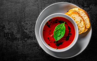 Fesleğenli domates çorbası koyu gri arka planda.