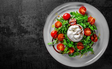 Burrata peynirli salata, roka salatası ve tabakta domates.