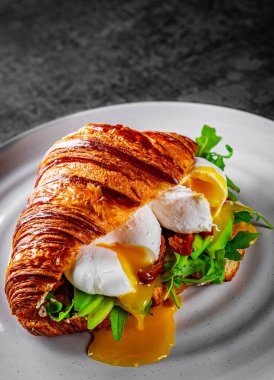 Kavrulmuş yumurta, domates ve avokadoyla birlikte kruvasan sandviçi.