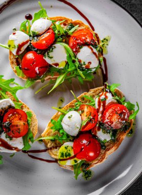 Kızarmış domatesli İtalyan bruschetta, mozzarella peyniri, balzamik sirke ve tabakta bitkiler.