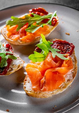 Somon balıklı bruschetta, vişneli domates, taze roka ve tabakta krem peynir.