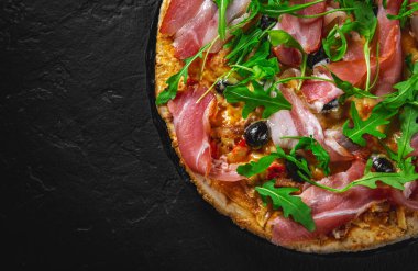 Mozzarella peynirli pizza, jambon, biber, zeytin, et, domates sosu, baharat ve taze roka. Koyu gri arka planda siyah tabakta İtalyan pizzası