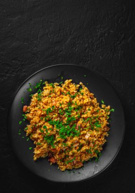 Sebzeli bulgur ve siyah tabaktaki et koyu gri arka planda.