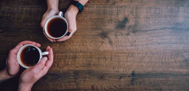 Kadın ve erkeklerin elinde bir fincan siyah çay ya da kahve. Tahta bir arka planda. Fotokopi alanı. en üstteki görünüm