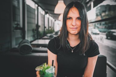 Genç kız elinde bardakla limonata kokteyli ve kafede içki tutuyor.