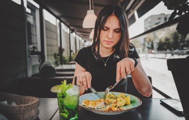 Çatal ve bıçak tutan kadın tabakta patates ve tavuk göğsü eti yiyor. 