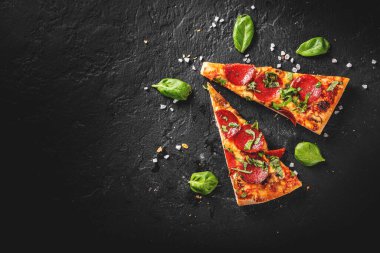  Mozzarella peynirli, salamlı, domates soslu, biberli, baharatlı iki dilim Pepperoni pizza. Koyu gri arka planda İtalyan pizzası