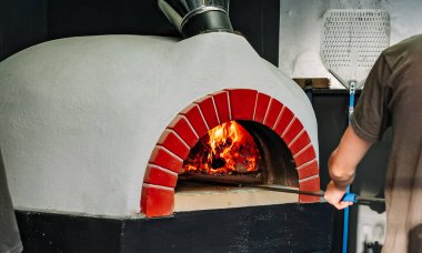 Şef pizza alır. İtalyan pizzası odun ateşinde pişirilir.
