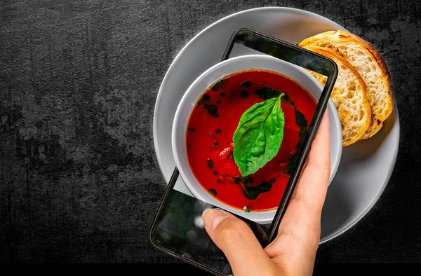 Kobieta Trzyma Pokazuje Smartfon Bierze Zupę Pomidorową Zdjęcie Bazylią Misce — Zdjęcie stockowe
