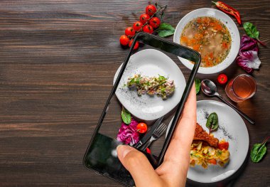 Kadın el ele tutuşuyor ve akıllı telefon gösteriyor. Masada üç çeşit fotoğraf çekiyor. Çorba, salata ve sebzeli tavuk gibi üç öğünden oluşan lezzetli öğle yemeği seti. yemek fotoğrafları