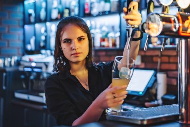 Bira musluğundaki kadın barmen barmen bardağa bira dolduruyor bir restoranda ya da barda servis yapıyor.