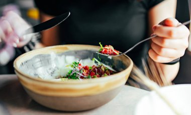 Elle et yiyen genç bir kadın bıçak ve çatal fom kasesi kullanıyor.