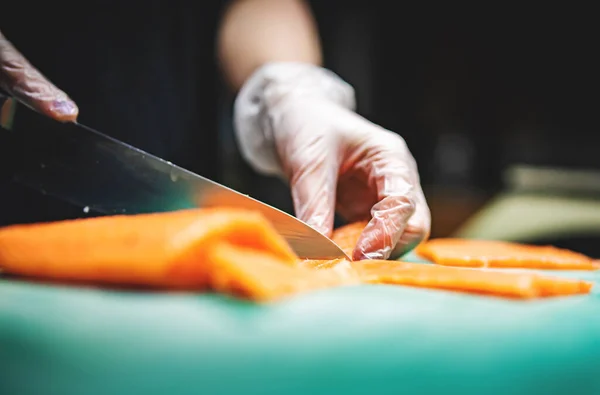 Close-up of hand sushi chef in gloves slices fresh salmon fish fillet at sushi bar.