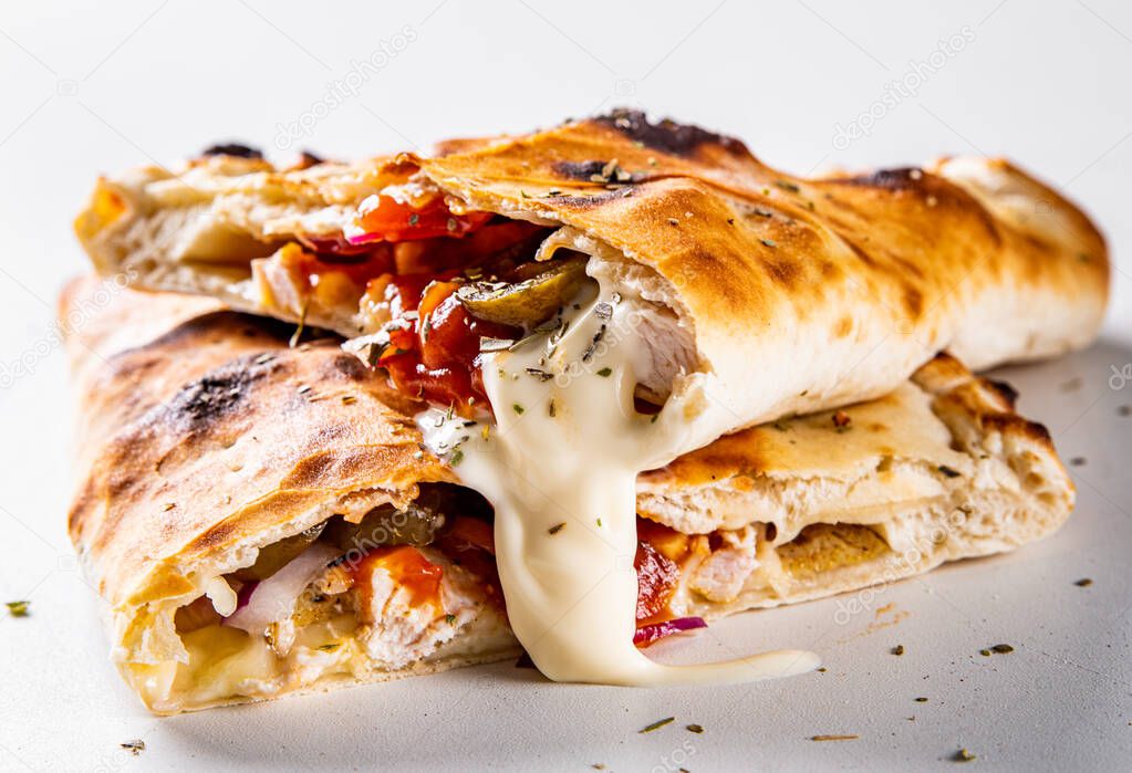calzone pizza folded in half with meat, vegetables and cheese on a white background