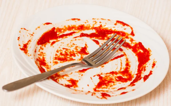 Placa sucia sobre la mesa. Salsa de tomate untada en un plato . — Foto de Stock