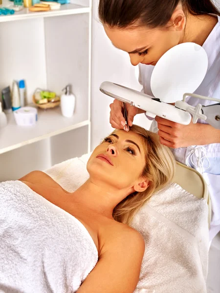 Woman middle-aged in spa salon. Tweezing eyebrow by beautician. — Stock Photo, Image