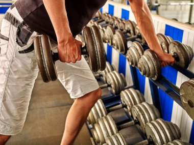 Kollarını dumbbells ile spor salonunda çalışan adam.