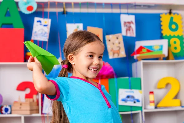 Niña divertida con avión de origami en el jardín de infantes . — Foto de Stock