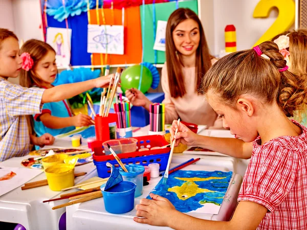 Τα παιδιά με δασκάλα γυναίκα ζωγραφική σε χαρτί στο νηπιαγωγείο . — Φωτογραφία Αρχείου