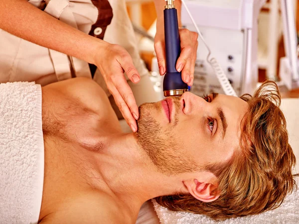 Hombre joven relajado recibiendo masaje facial eléctrico . — Foto de Stock