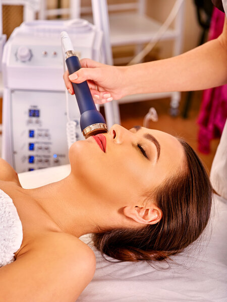 Relaxed young woman receiving electric facial massage.