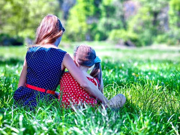 Lányok viselt piros és kék pöttyös ruha ül a zöld fű-ba Park. — Stock Fotó