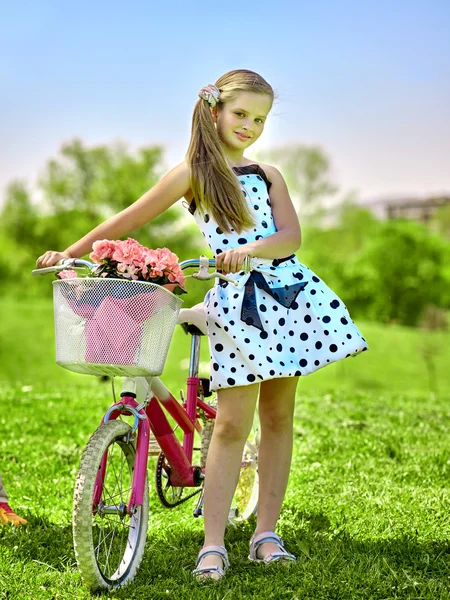 Child girl wearing white polka dots dress rides bicycle into park. — Stock Photo, Image