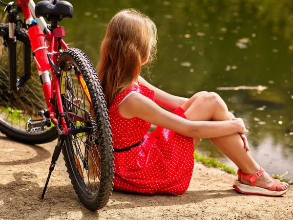 Bikes cycling girl into park. Girl sits leaning on  bicycle on shore. — Stock Photo, Image