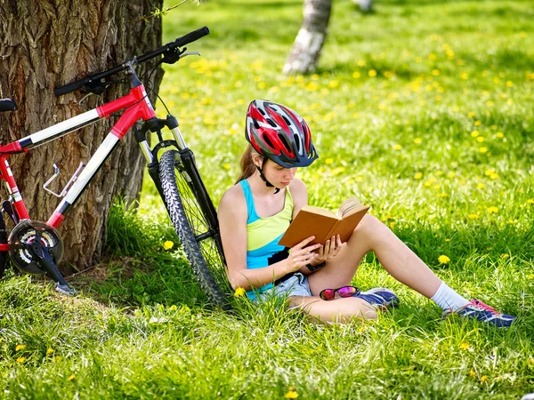 Cyklar cykling flickan bär hjälm läsa bok om vila nära cykel. . — Stockfoto