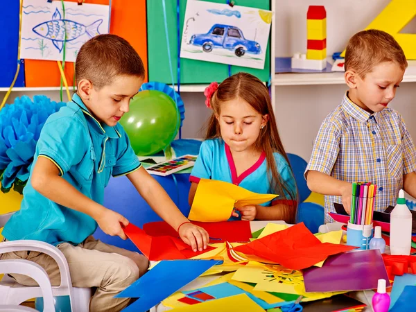 Kinderen houden gekleurd papier op tafel in de kleuterschool . — Stockfoto
