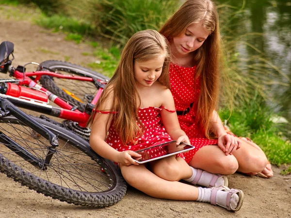 Ποδήλατα, ποδηλασία κορίτσι σε πάρκο. Παρακολουθούν τα παιδιά pc ταμπλετών. — Φωτογραφία Αρχείου